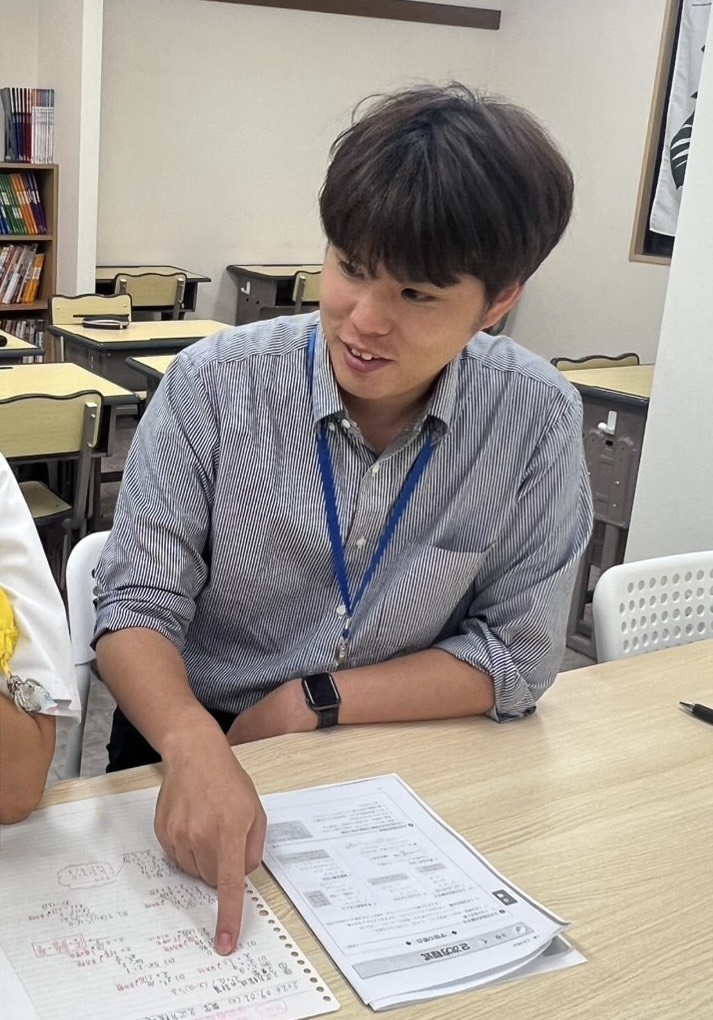 野村先生が教室で生徒の教材を示しながら説明する様子